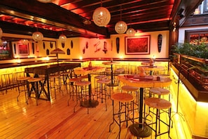 Interior de un restaurante con mesas redondas, taburetes de bar y lámparas esféricas colgantes.