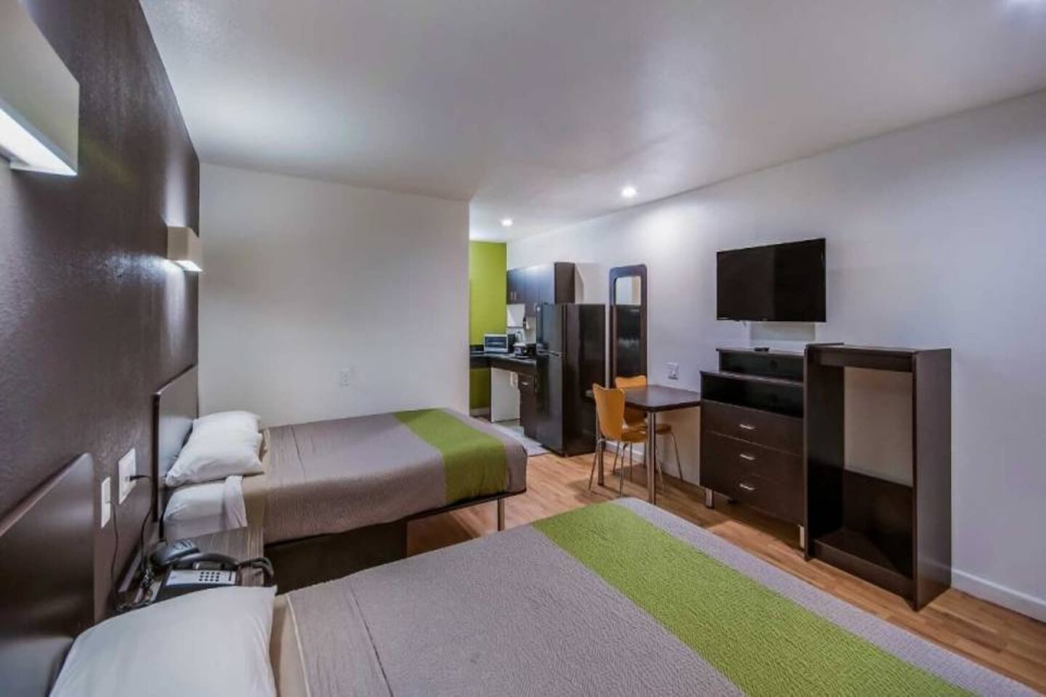 Ein kleines Hotelzimmer mit zwei Einzelbetten, einem Schreibtisch, einem Stuhl, einem Fernseher und einer Küchenzeile.