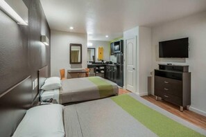 A compact hotel room with a bed, a desk, a chair, a television, and a kitchenette.