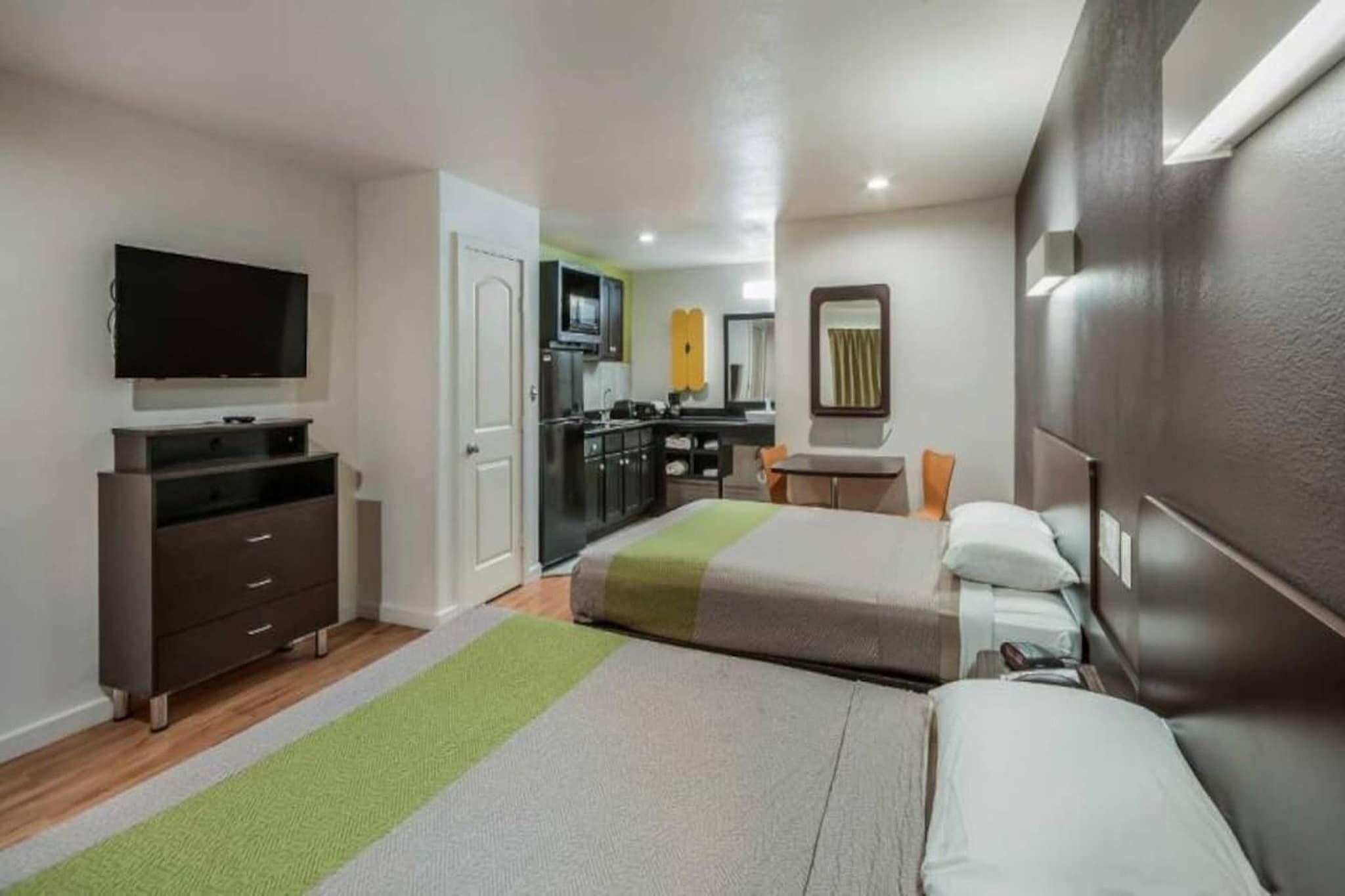 A hotel room with a bed, a desk, a television, and a kitchenette.