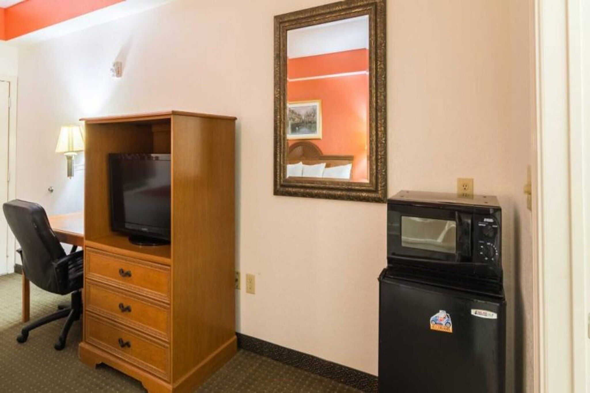 Une chambre d’hôtel équipée d’une commode en bois, d’une télévision, d’un four à micro-ondes et d’un bureau avec une chaise.