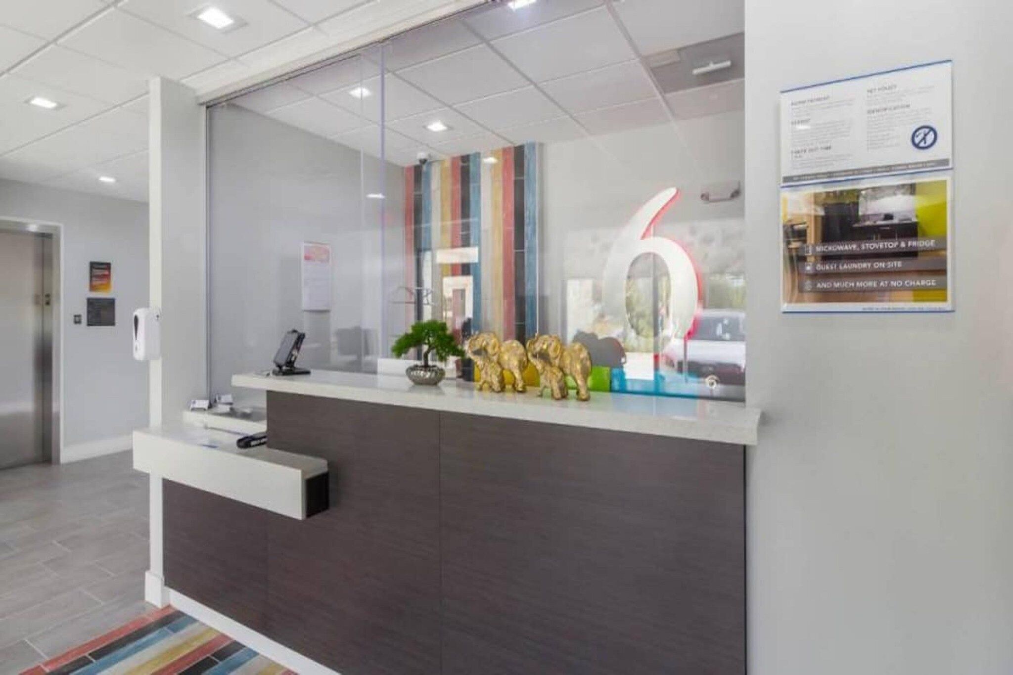 A reception desk with a glass partition, a digital screen, and a poster on the wall.
