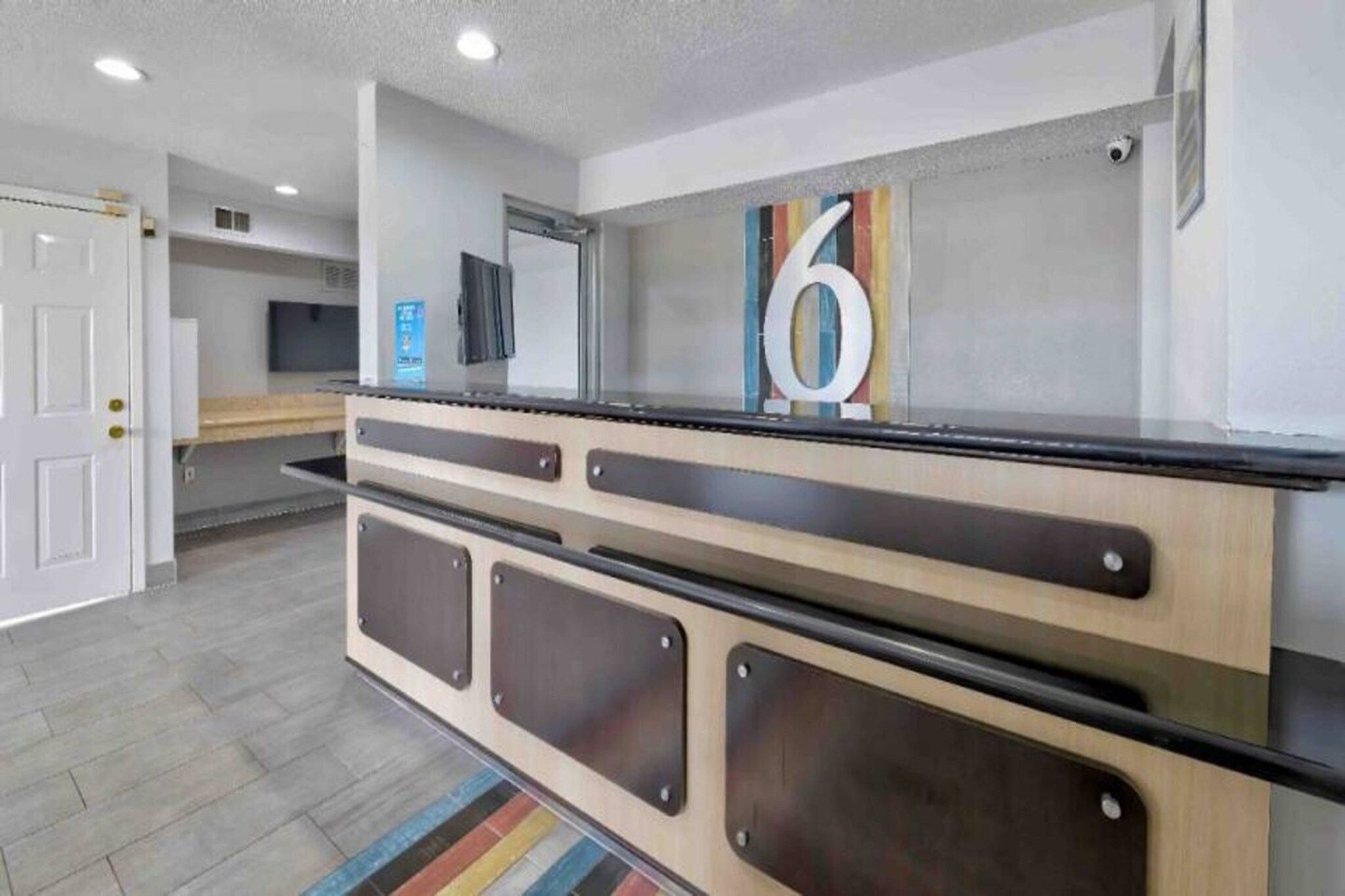 A reception desk with a number '6' sign, a flat-screen TV, and a security camera.