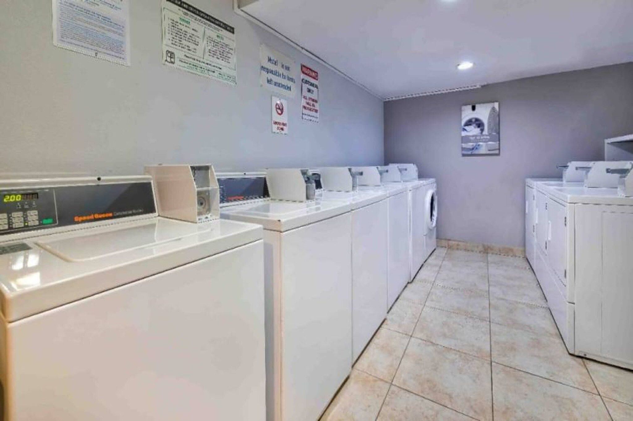 A laundry facility with multiple washing machines and dryers, a digital control panel, and informational posters on the walls.