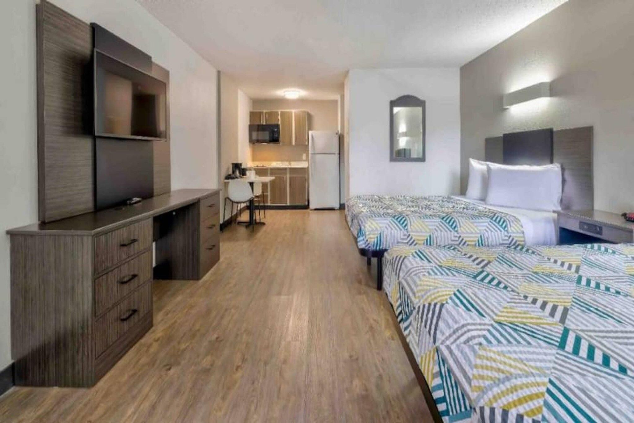 A hotel room with a bed, a desk, a chair, a TV, and a kitchenette.
