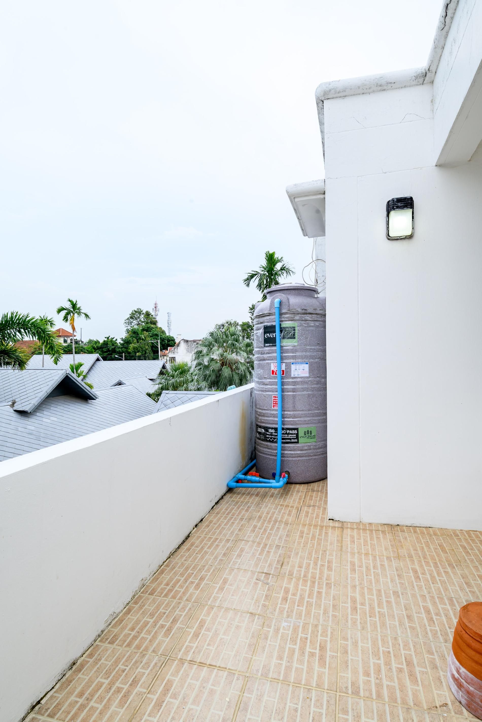 A rooftop terrace with a water tank, a blue hose, and a tiled floor.