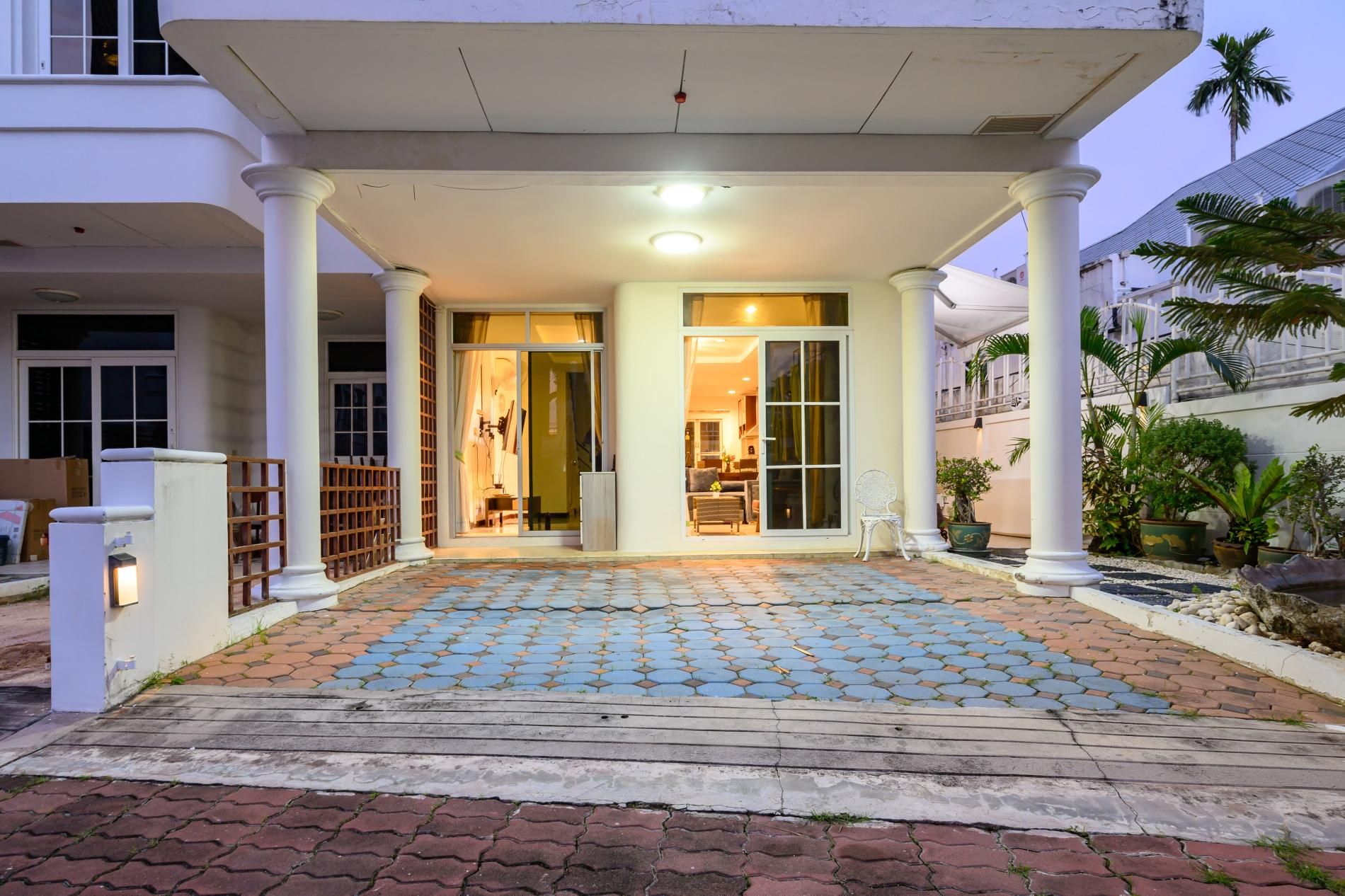 A hotel entrance with a covered porch, a tiled walkway, and a palm tree in the background.