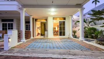 A hotel entrance with a covered porch, a tiled walkway, and a palm tree in the background.