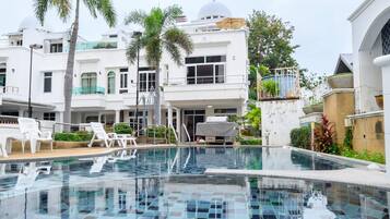 Ein Pool mit Kachelboden, umgeben von Palmen und einem Gebäude mit weißer Fassade.