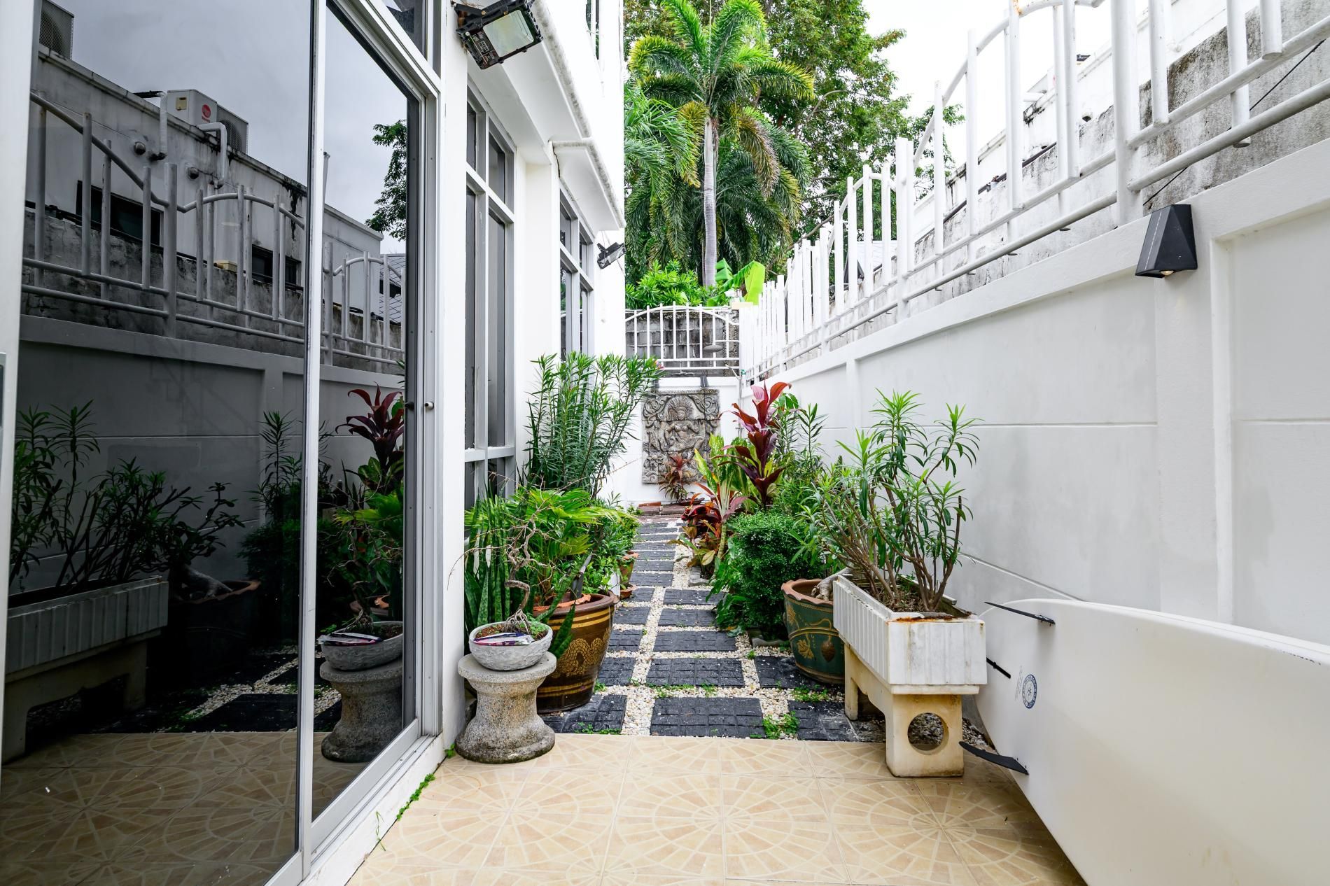 A narrow courtyard with a tiled floor, potted plants, and a staircase leading to a balcony.