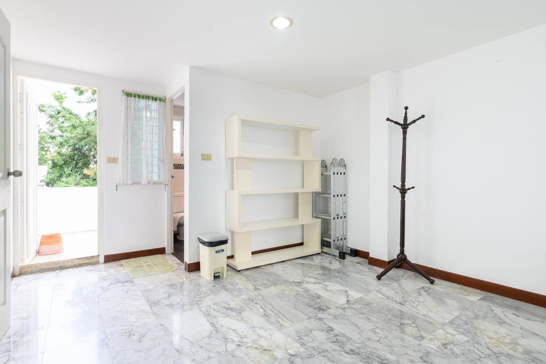 A hallway with a marble floor, a coat rack, a white shelf unit, and a door leading to an outdoor area.