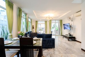 Uma sala de jantar moderna com piso de mármore, uma mesa posta para dois e um sofá azul escuro ao fundo.