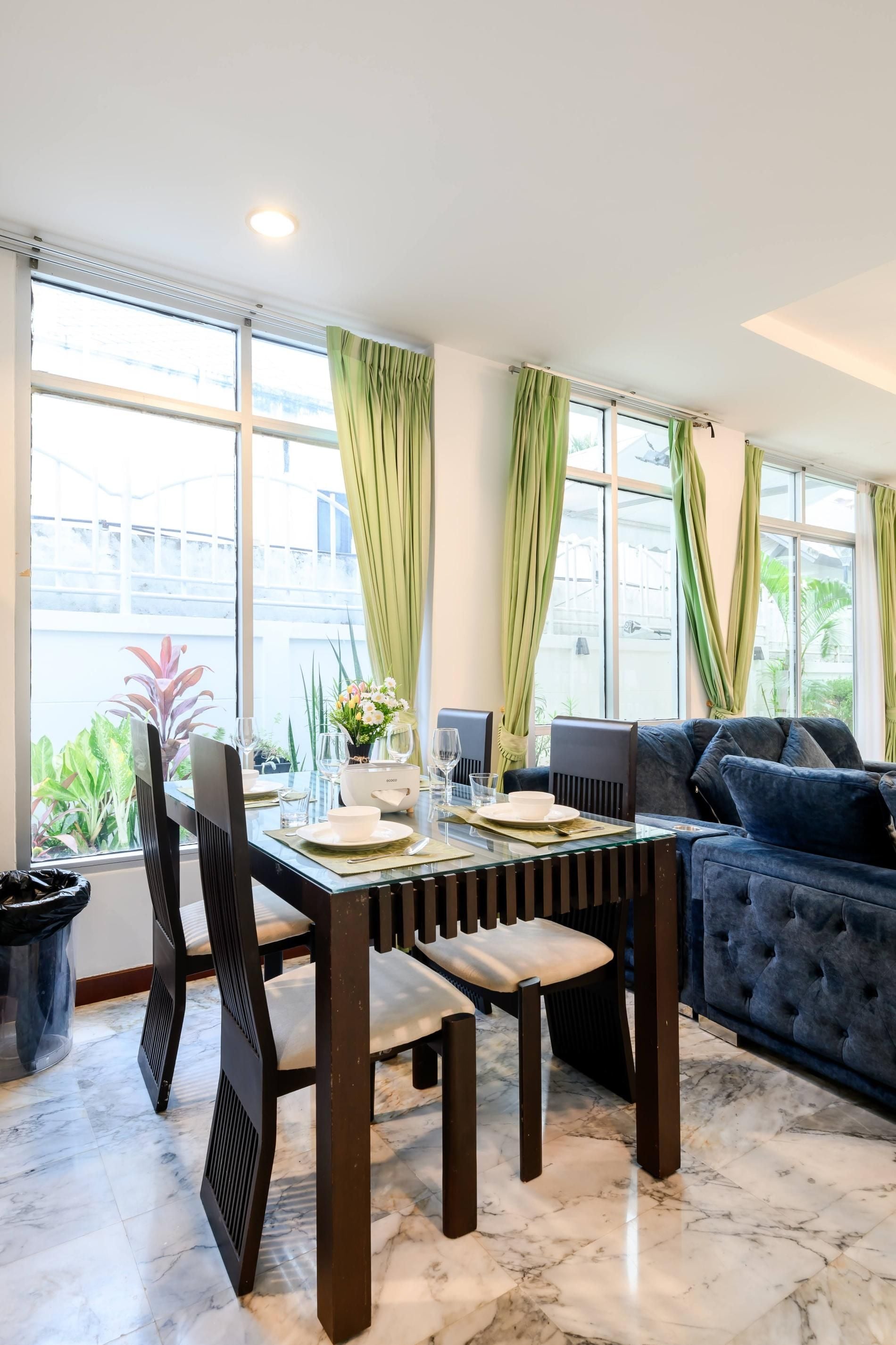 A dining area with a table set for four, a sofa, and a view of the outdoors through large windows.
