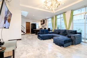 A modern living room with a sectional sofa, a glass coffee table, and a large window with curtains. - Wongamat 3BR Townhouse near Beach (NP1) (Bang Lamung,)