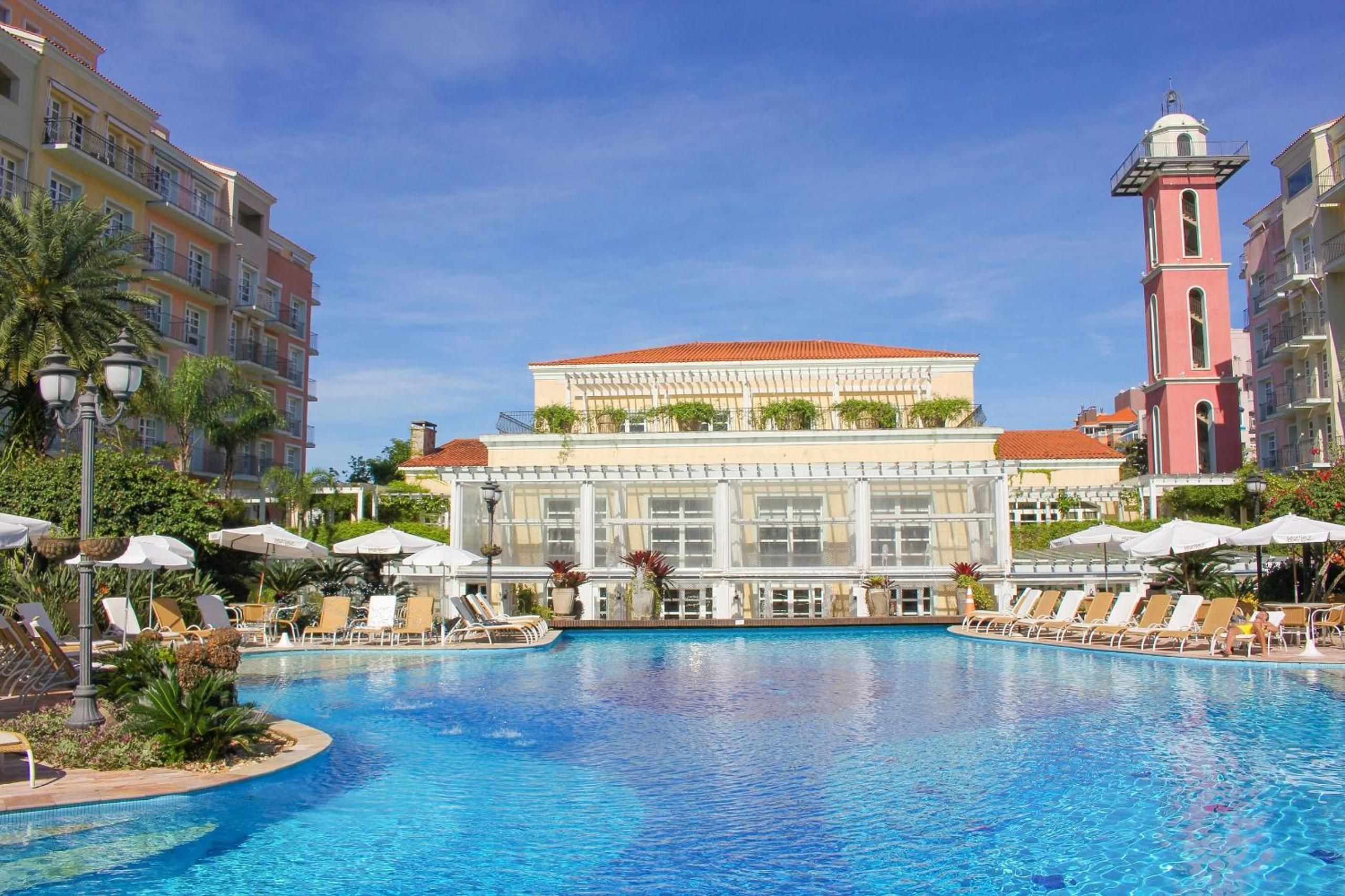 A swimming pool with lounge chairs and umbrellas, surrounded by multi-story buildings with balconies.