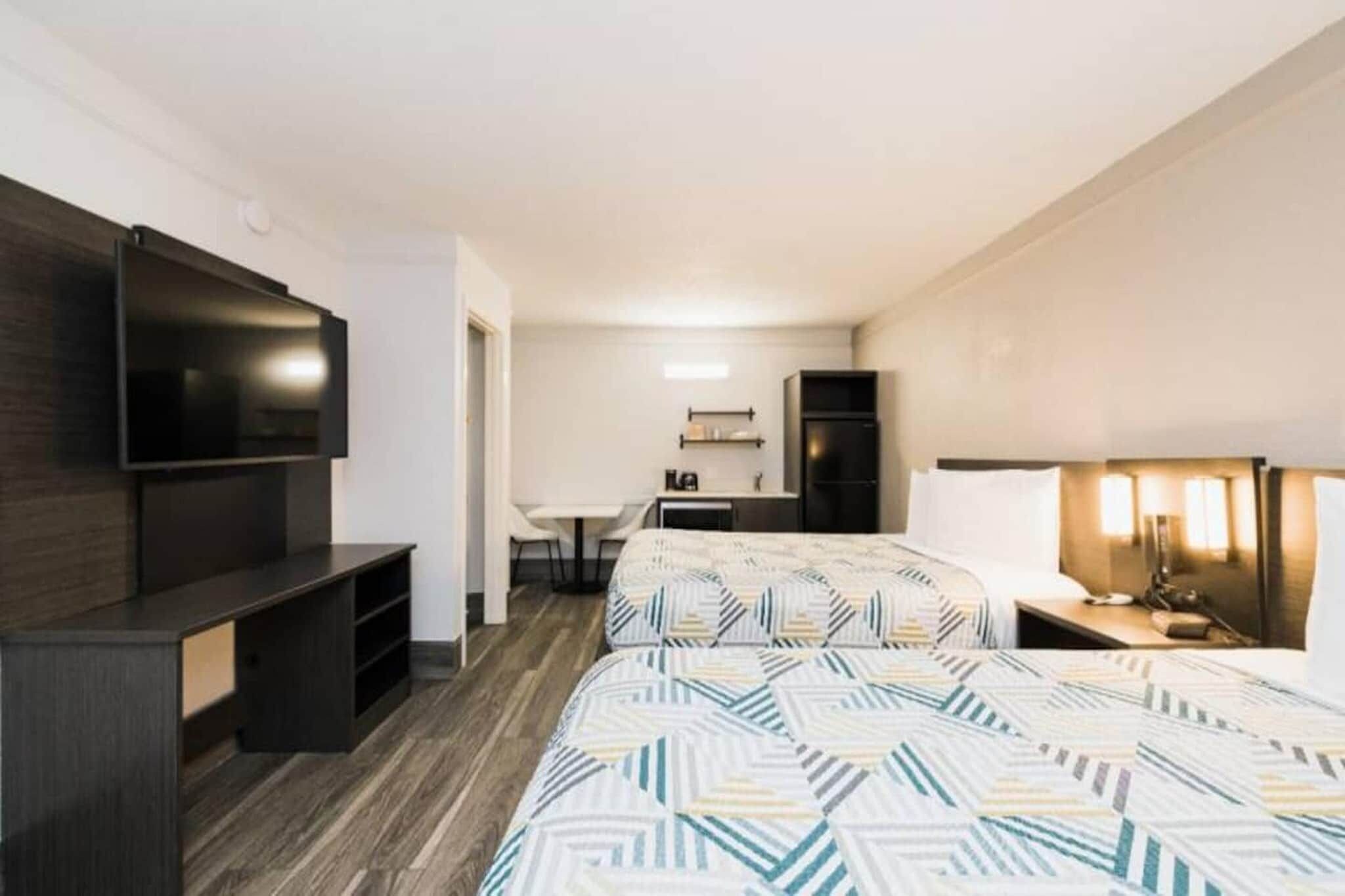 A hotel room with two beds, a TV, a desk, and a chair.
