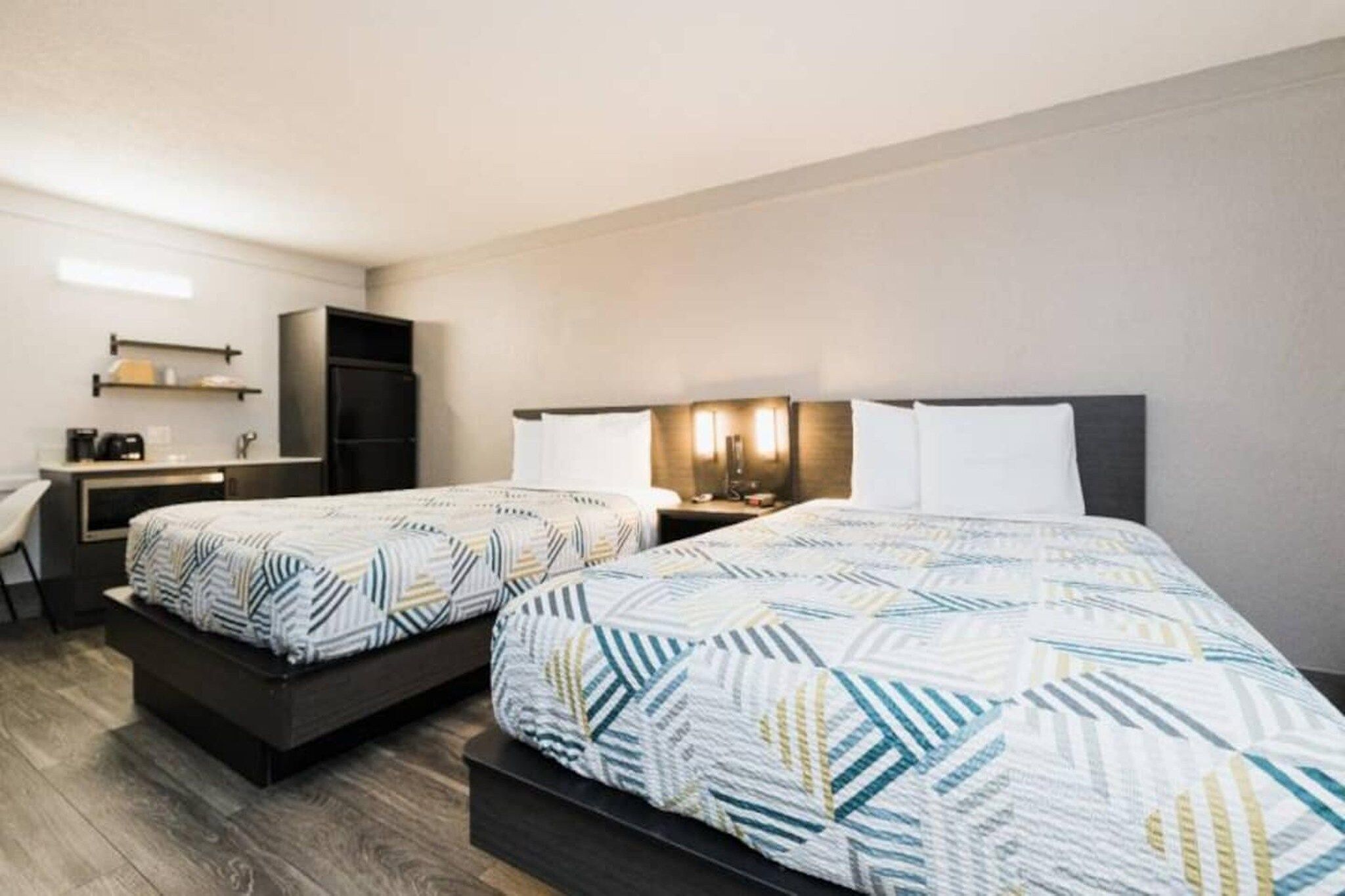 A hotel room with two beds, a desk, a chair, and a refrigerator.