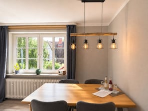 Ein Essbereich mit einem Holztisch, vier Stühlen, einem Fenster mit Vorhängen und Pendelleuchten.