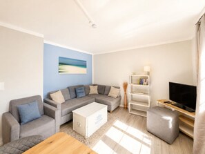 A modern living room with a grey sectional sofa, a white coffee table, a bookshelf, and a flat-screen TV. - Holiday Apartment With 1 Bedroom (Wyk auf Foehr)