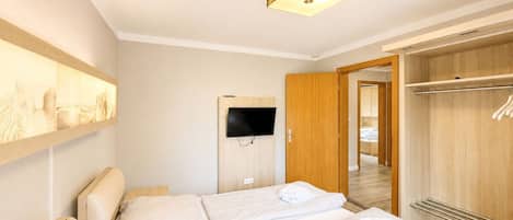 Een hotelkamer met twee bedden, een wandtelevisie, een houten kledingkast en een gang naar een andere kamer.