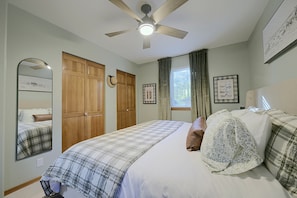 Une chambre à coucher avec un lit, un ventilateur de plafond, une armoire et une fenêtre avec des rideaux.
