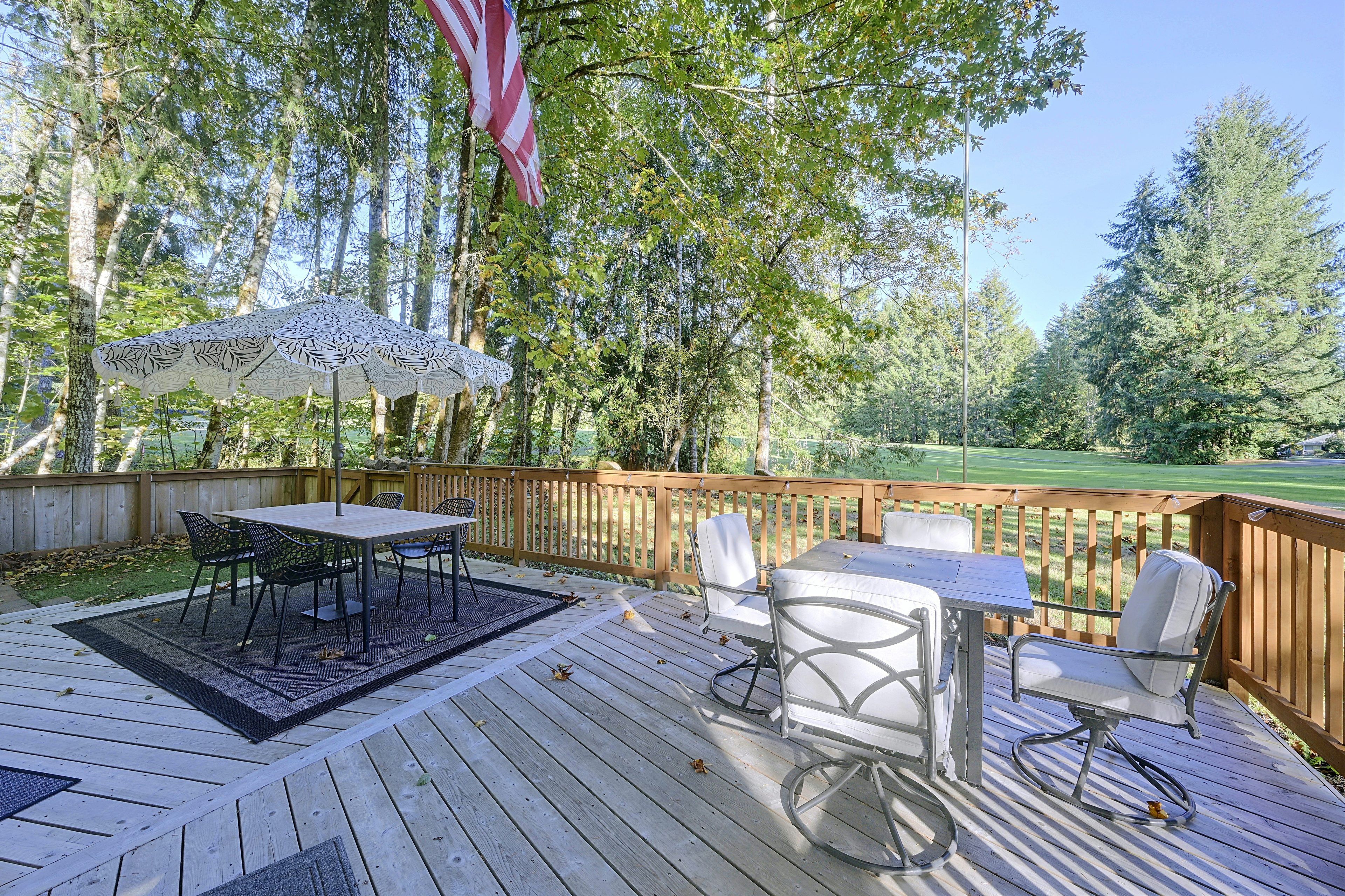 Um deck de madeira com mesa e cadeiras, uma bandeira americana e vista para um campo de golfe.