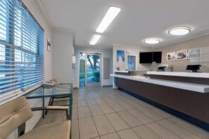 A reception area with a glass partition, a reception desk, a flat-screen TV, and a door leading outside. - 2 Queen Beds | Non-Smoking (North Richland Hills)