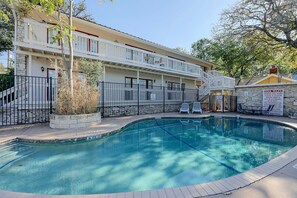 A swimming pool with a stone wall, a covered deck, and a sign indicating pool rules. - Walkable West 6th Condo w/ Pool & Porch (Austin)