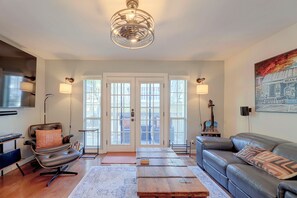 A living room with a sofa, a chair, a coffee table, and a television. There is a door with glass panels and a painting on the wall. - Walkable West 6th Condo w/ Pool & Porch (Austin)