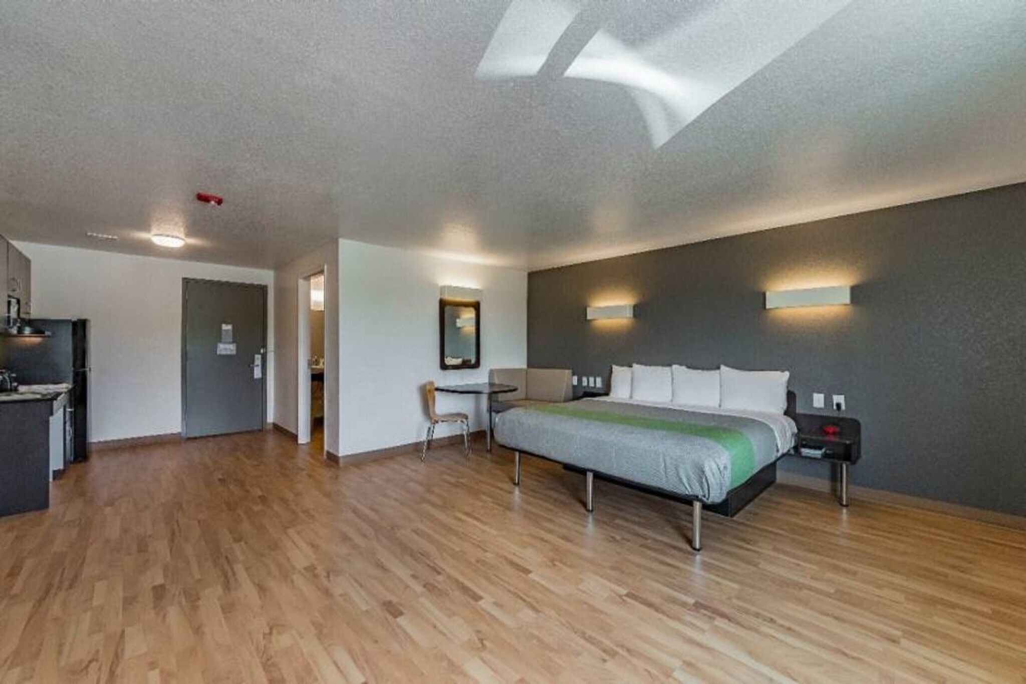 A modern hotel room with a large bed, a desk, and a kitchenette.