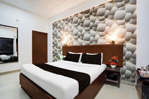 A modern hotel room with a large bed, a wooden headboard, a decorative wall, a bedside table with a lamp, and a small plant. - Collection O Tourist Complex Area (Agra)