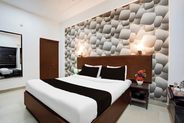 A modern hotel room with a large bed, a wooden headboard, a decorative wall, a bedside table with a lamp, and a small plant. - Collection O Tourist Complex Area (Agra)