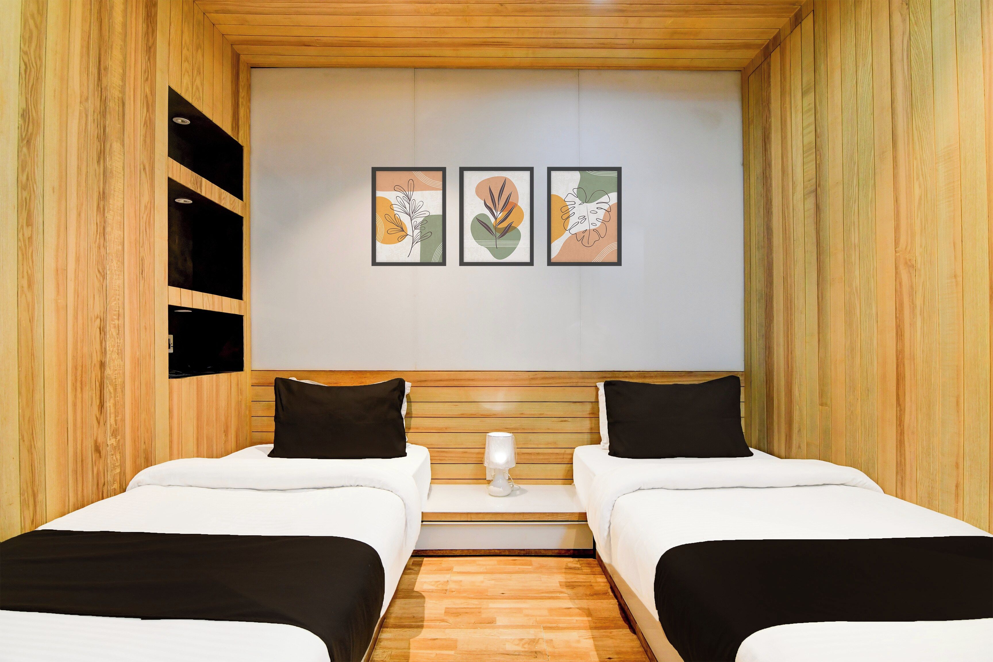 A hotel room with two beds, a wooden headboard, a small bedside table, and three framed artworks on the wall.