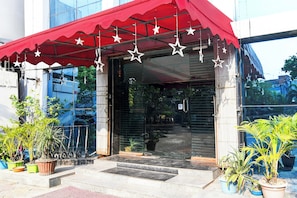 Entrada de un edificio con un toldo rojo, adornos con estrellas y plantas en macetas.