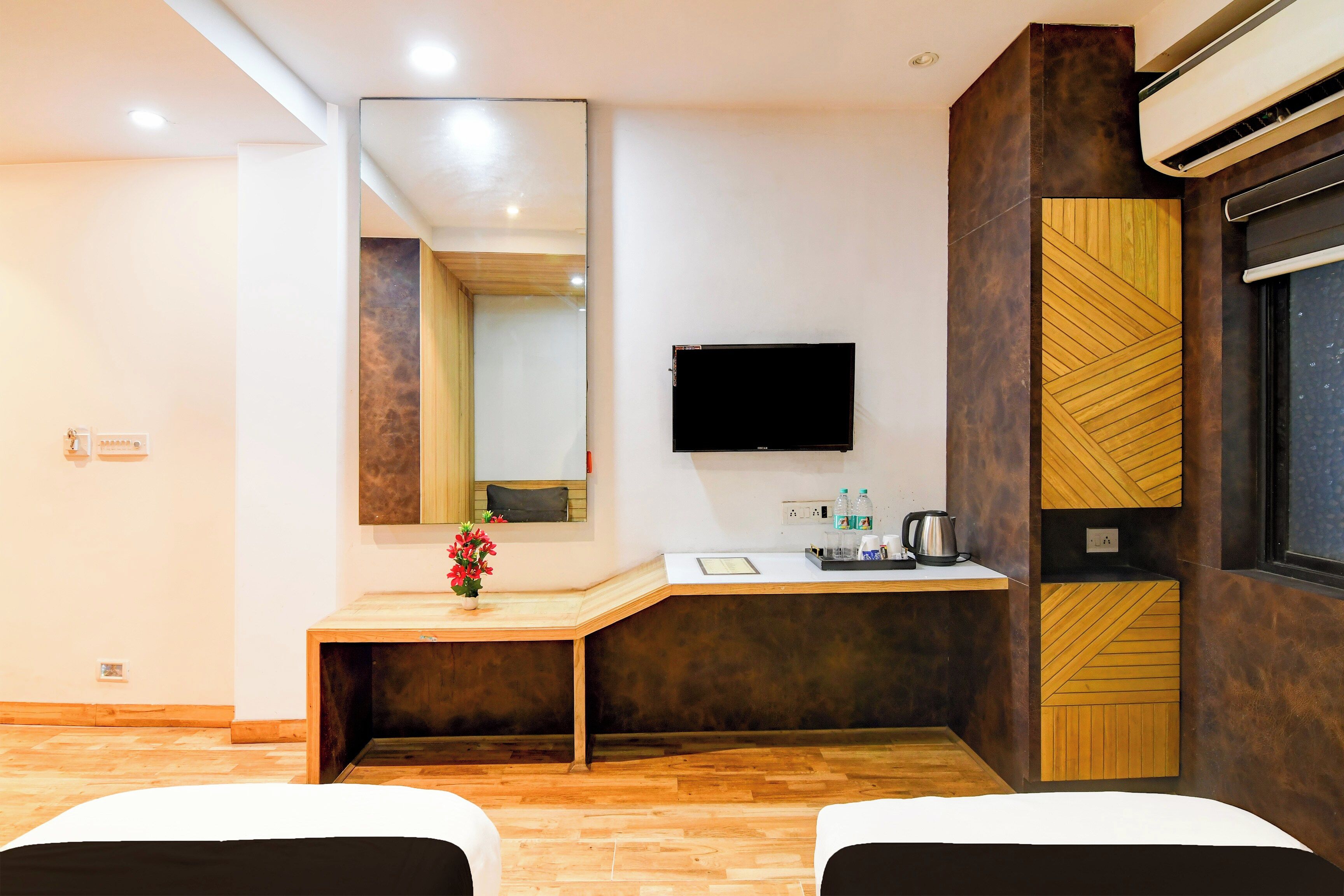 A hotel room with a wooden floor, a desk with a mirror, a flat-screen TV, a wooden cabinet, and two beds.