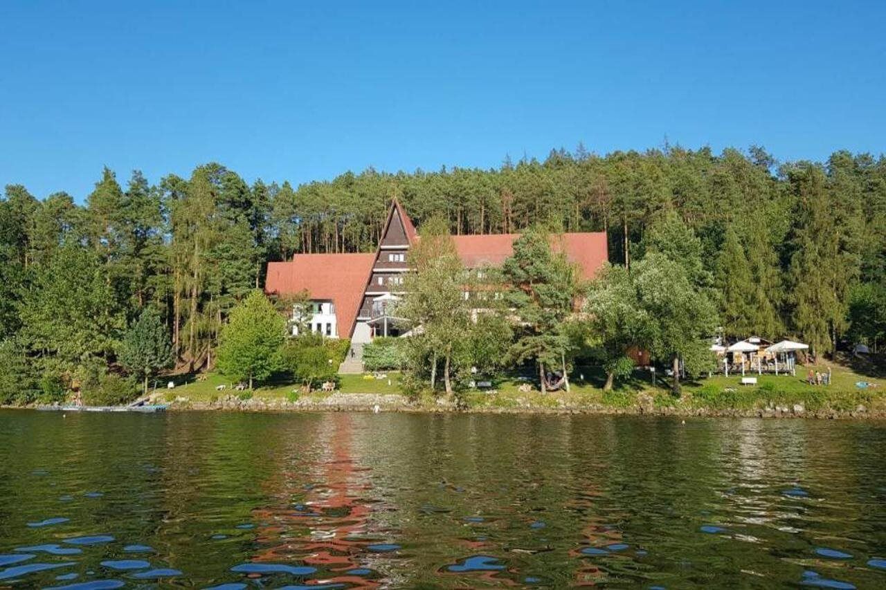A lakeside property with a prominent red-roofed building, surrounded by dense forest and a calm lake.