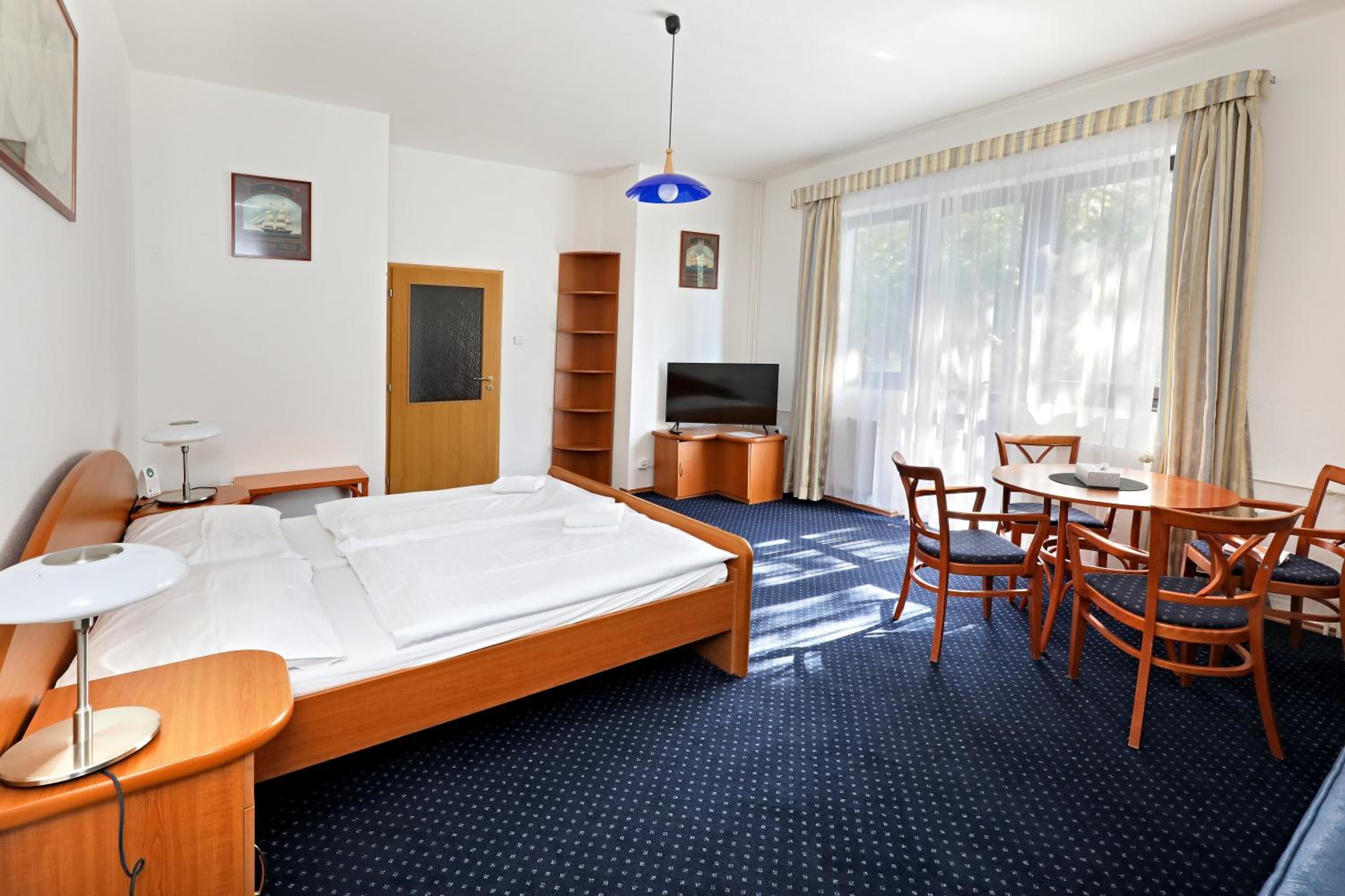 A hotel room with a bed, a desk, a chair, a television, and a window with curtains.