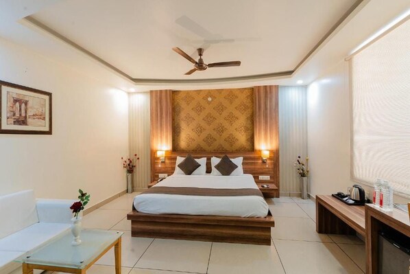 A hotel room with a bed, bedside tables, a desk, a chair, a ceiling fan, and a wall-mounted artwork. - Hotel Signature inn (Jaipur)