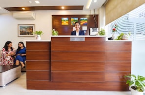 A reception desk with a 'RECEPTION' sign, a receptionist, and two guests seated on a sofa. - Hotel Signature inn (Jaipur)