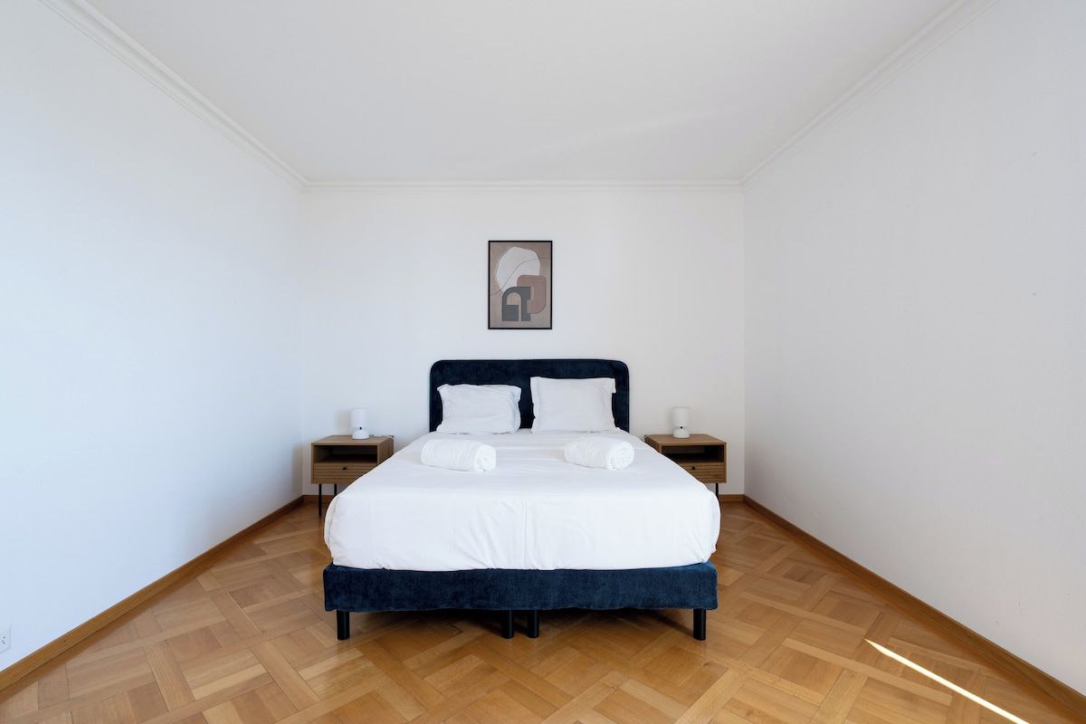 Ein Schlafzimmer mit einem Bett, zwei Nachttischen, einem gerahmten Bild an der Wand und Holzboden.