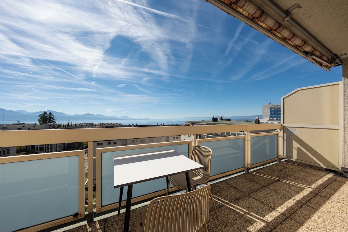 Ein Balkon mit Tisch und Stühlen mit Blick auf eine Stadtlandschaft, in der Ferne Berge.