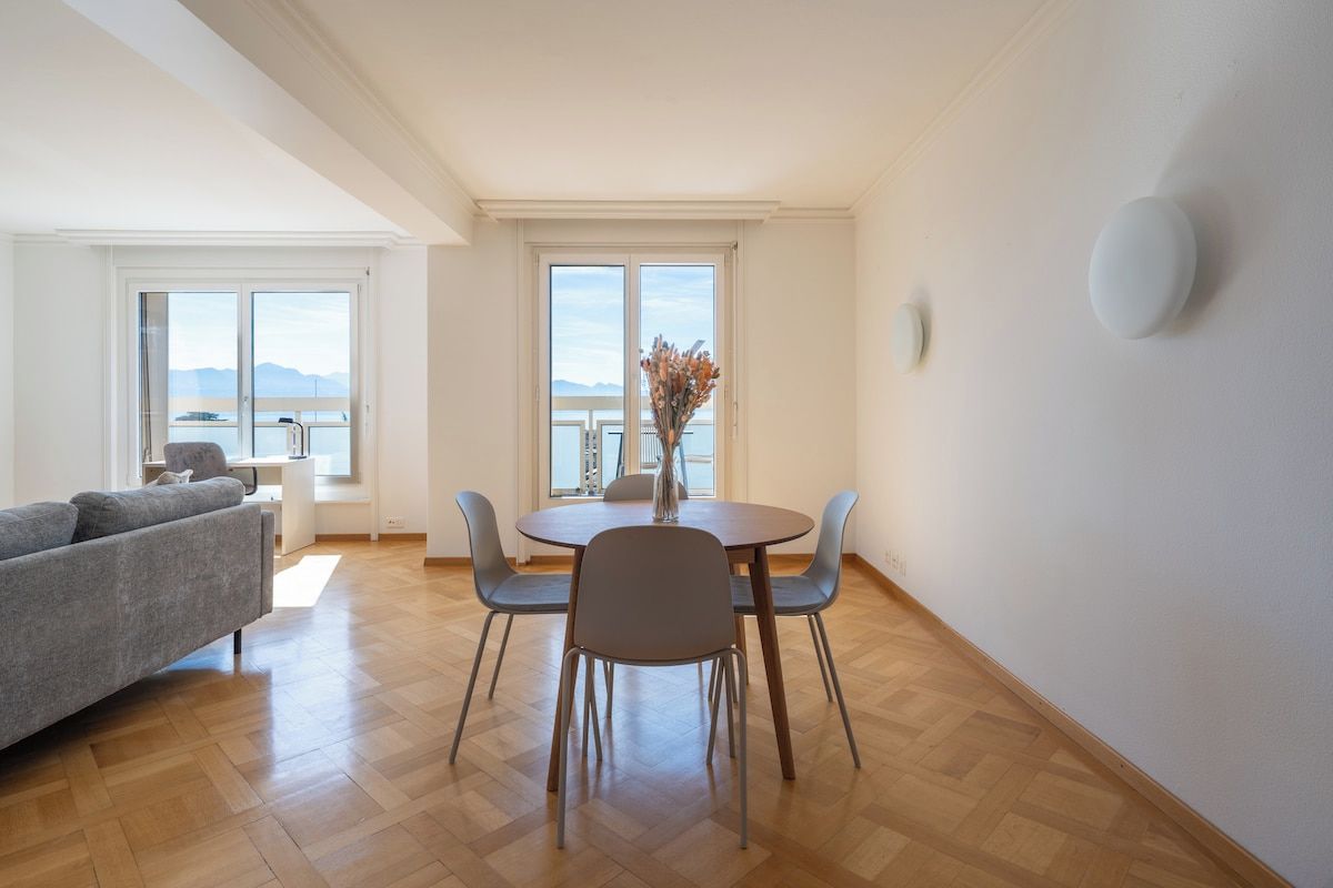 A modern living room with a dining area, large windows, and a view of the sea.