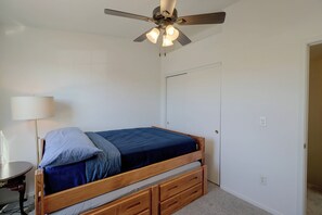 Ein Schlafzimmer mit einem Einzelbett, einem Deckenventilator, einem Nachttisch und einer Lampe.