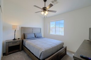 A bedroom with a bed, nightstand, lamp, ceiling fan, window, and a TV stand. - Extended Stay Ready! Sparkis Townhome w/ Patio (Sparks)