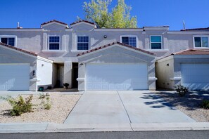 A two-story residential building with a garage entrance, a driveway, and a small garden area. - Extended Stay Ready! Sparkis Townhome w/ Patio (Sparks)