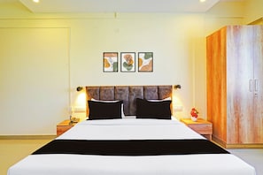 A hotel room with a large bed, two bedside tables, a wardrobe, and three framed artworks on the wall.
