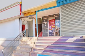 Entrada de un hotel con una escalera que sube hasta el cuarto piso, una puerta persiana cerrada y un cartel que anuncia suites indias.