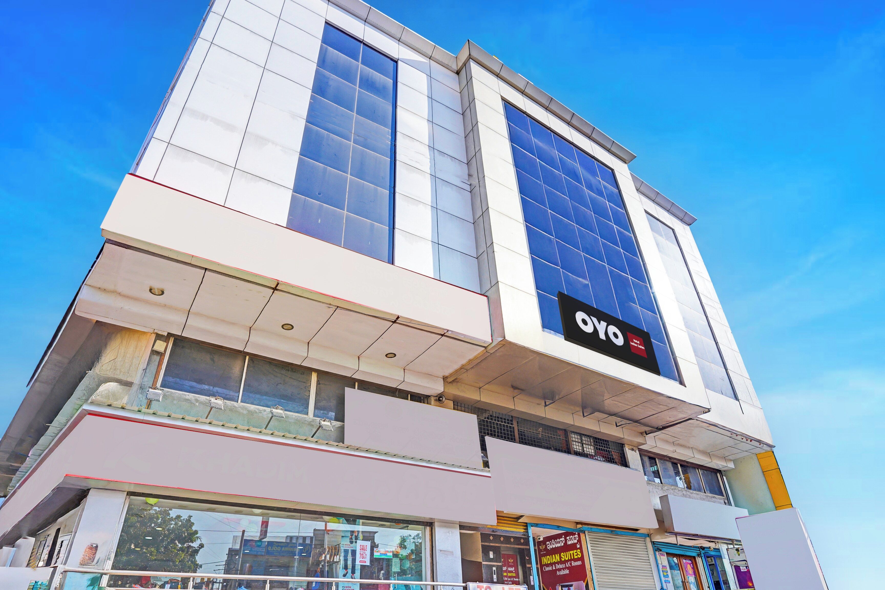 A modern hotel building with a prominent 'OYO' sign, large windows, and a clear sky.