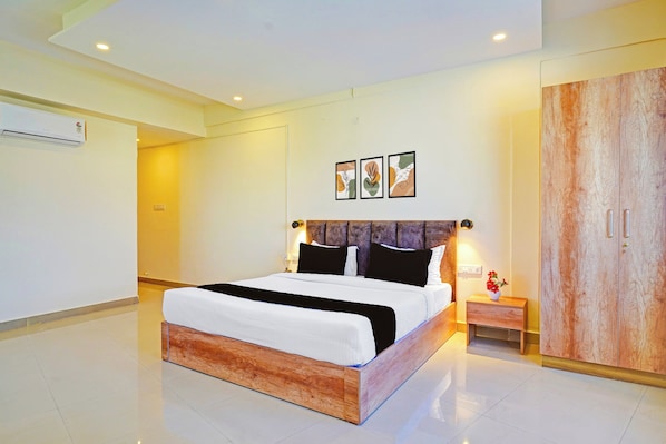 Una habitación de hotel moderna con una cama grande, un cabecero de madera, un armario y una mesita de noche con una lámpara.