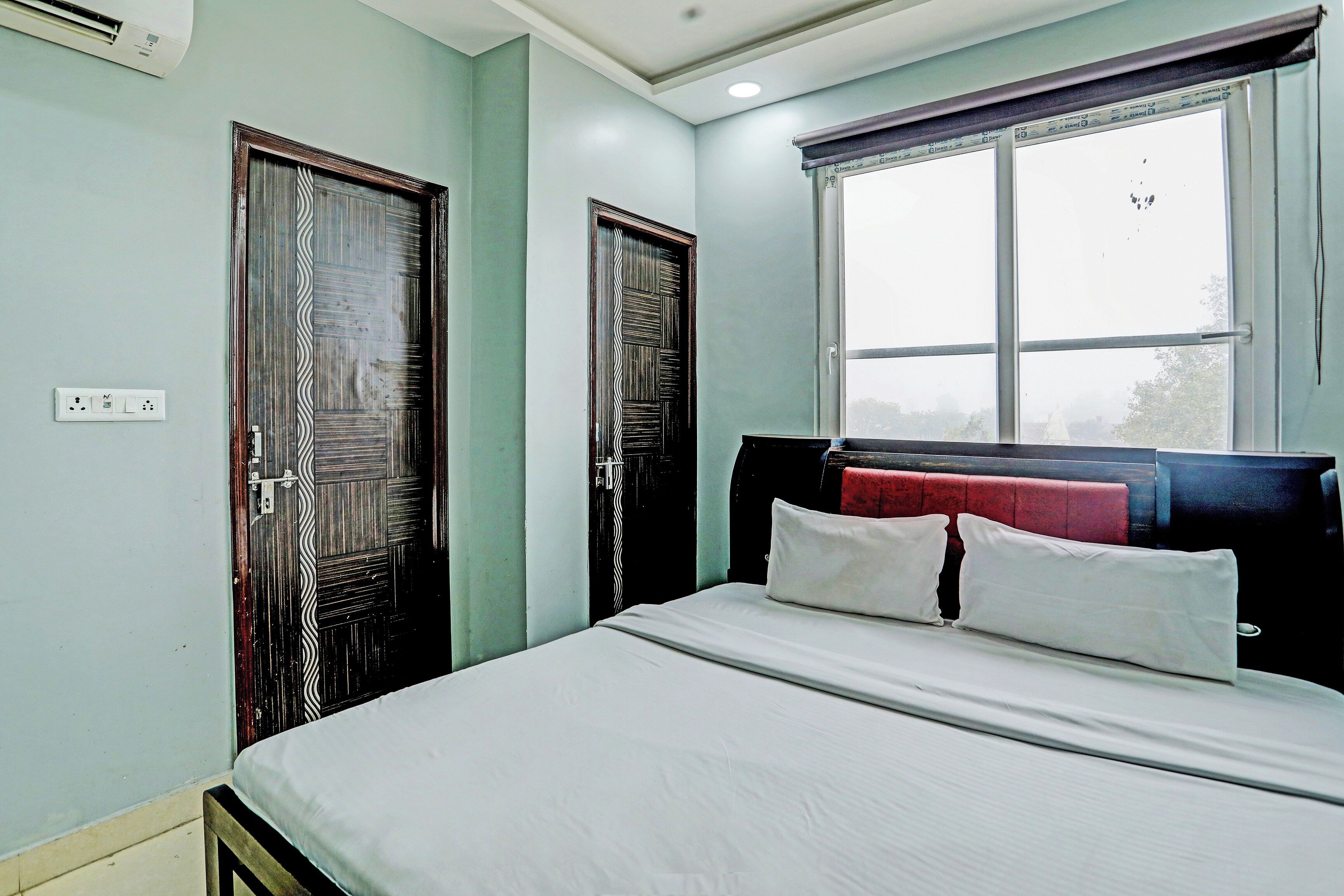 Un dormitorio con cama, dos puertas, una ventana y un enchufe.